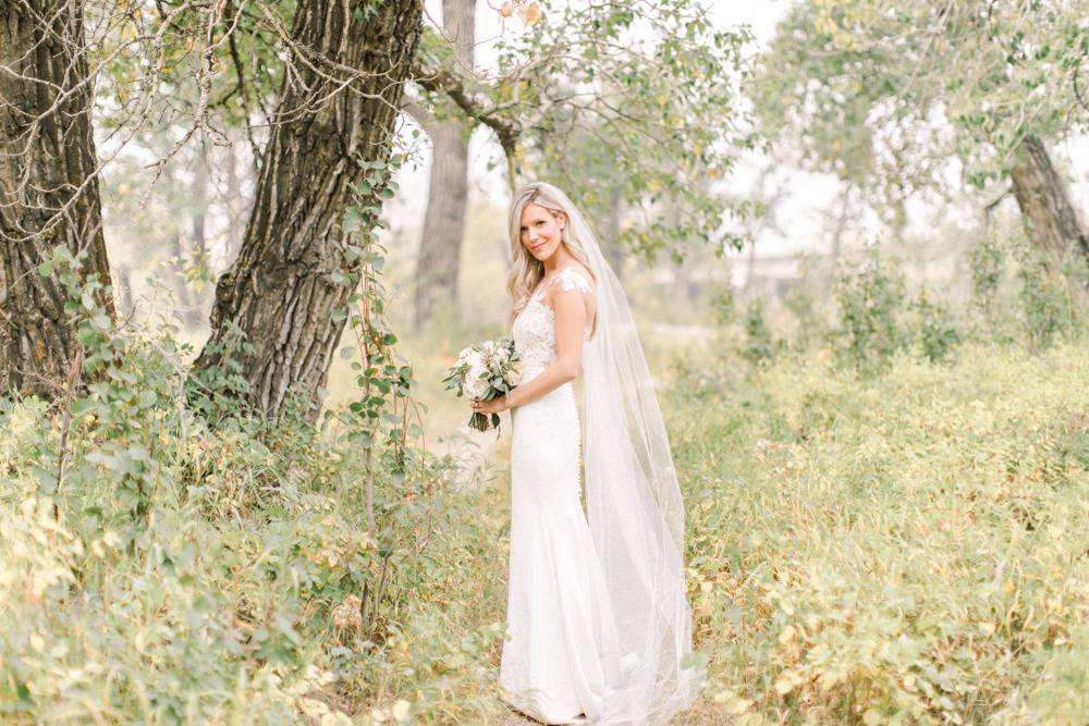 wide shot of the bride in nature with her bouquet at the lake house in Calgary
