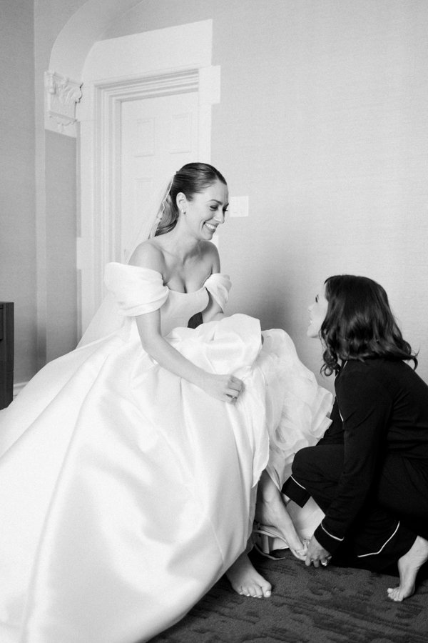 black and white photo of bride getting help putting on her wedding day shoes at the Calgary Fairmont Palliser Hotel