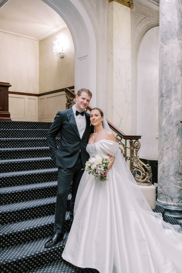 wide shot of bride and groom standing on grand stair case looking at the camera at the Calgary Fairmont Palliser Hotel