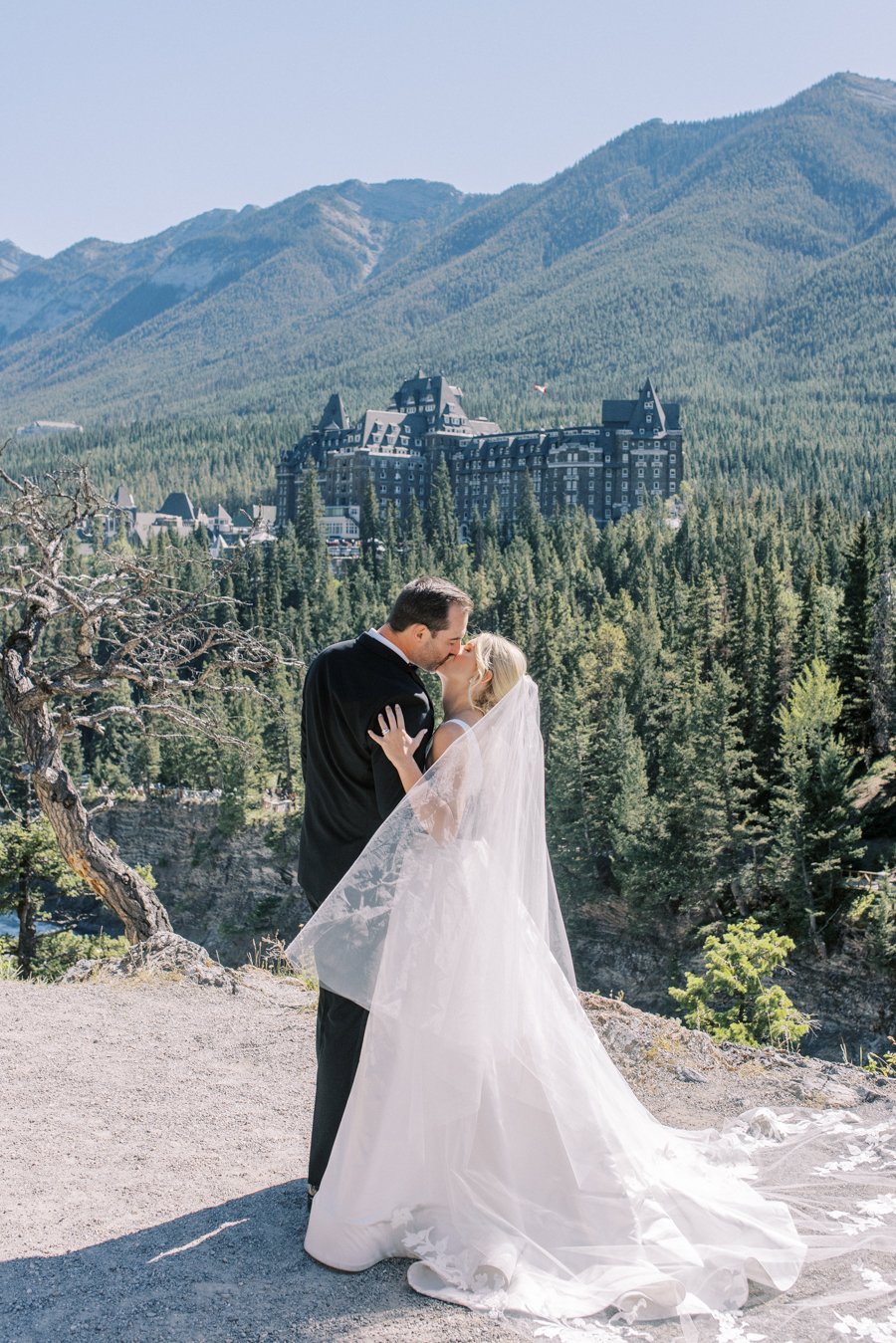 wide shot of bride and groom kissing at surprise corner in Banff Alberta with the fairmont banff springs in the background