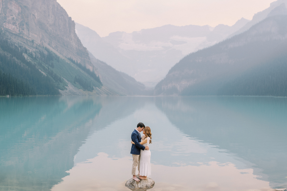 couple standing on a rock in the water on the shore of Lake Louise photographed by Lake Louise Wedding Photographers Heidrich Photography
